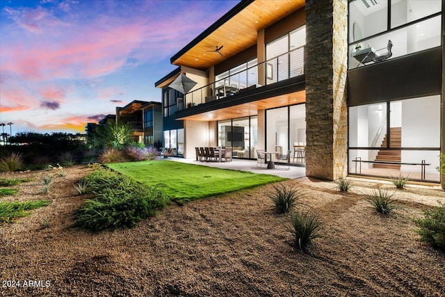 back house at dusk featuring a yard, a balcony, and a patio