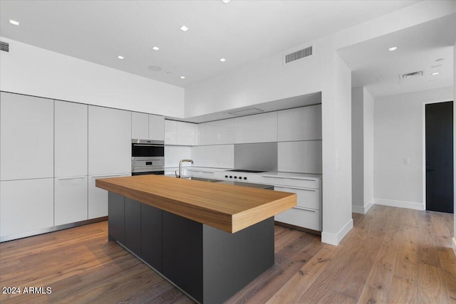 kitchen with white cabinets, a spacious island, sink, light hardwood / wood-style floors, and stainless steel double oven