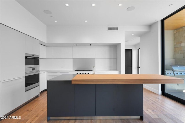 kitchen with light hardwood / wood-style floors, a kitchen island, white cabinetry, and stainless steel double oven