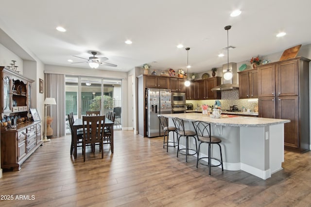 kitchen with pendant lighting, decorative backsplash, a kitchen island with sink, light stone counters, and stainless steel appliances