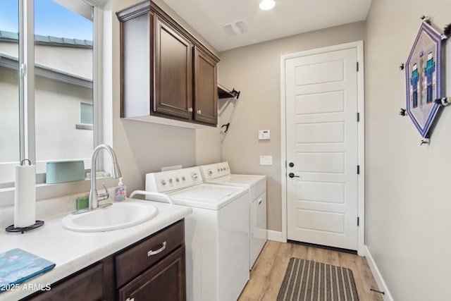 clothes washing area featuring independent washer and dryer, cabinets, sink, and light wood-type flooring