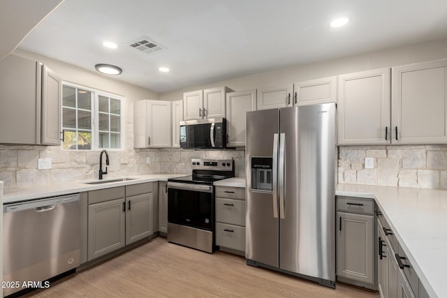 kitchen featuring visible vents, gray cabinetry, light wood-style floors, stainless steel appliances, and a sink