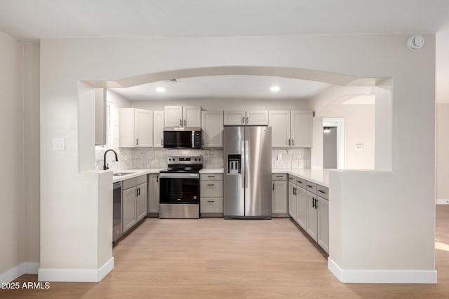 kitchen featuring arched walkways, stainless steel appliances, light wood-style floors, and a sink