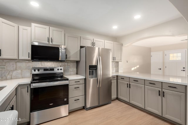 kitchen featuring decorative backsplash, gray cabinets, a peninsula, and stainless steel appliances