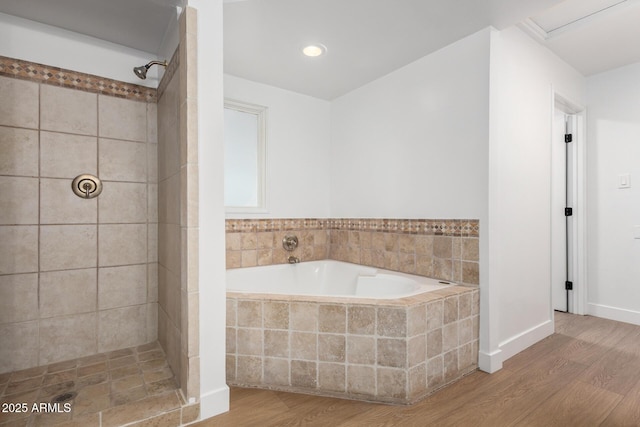 bathroom with a garden tub, wood finished floors, baseboards, and tiled shower