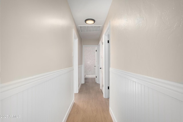 hallway with visible vents, light wood-style flooring, and wainscoting