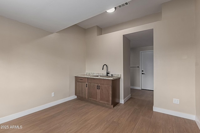 bar featuring light wood finished floors, visible vents, baseboards, and a sink