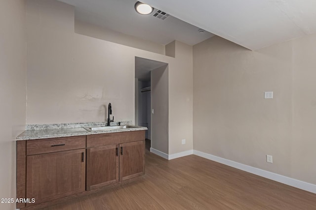 bar with visible vents, light wood-type flooring, baseboards, and a sink