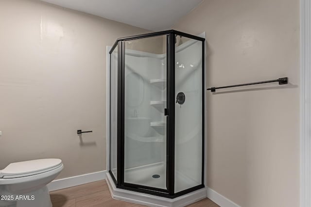 bathroom with a shower stall, toilet, baseboards, and wood finished floors