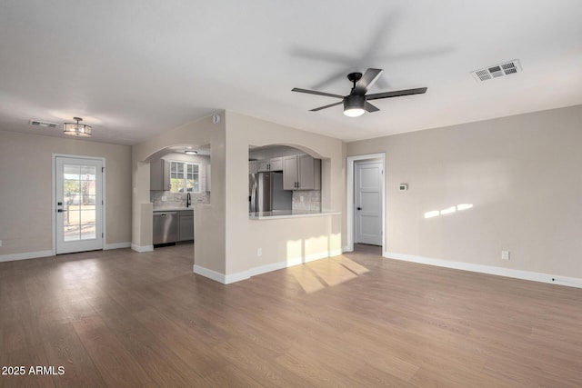 unfurnished living room with baseboards, wood finished floors, visible vents, and arched walkways