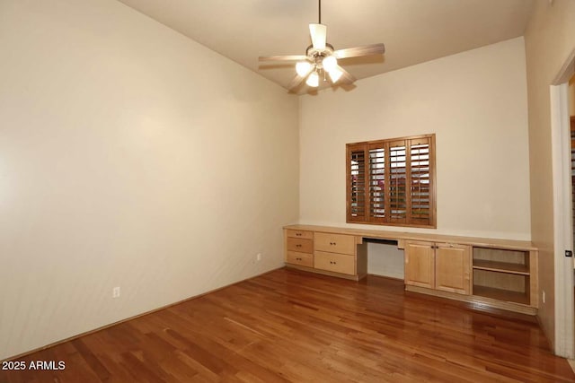 unfurnished office with built in desk, wood finished floors, and a ceiling fan