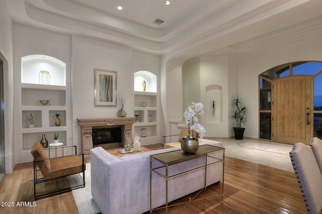 living area featuring built in features, recessed lighting, visible vents, a high end fireplace, and wood finished floors