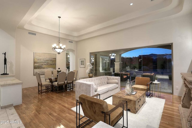 living room featuring visible vents, a tray ceiling, a notable chandelier, and wood finished floors