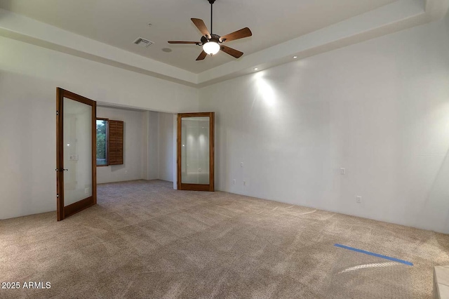 unfurnished room featuring carpet, visible vents, a ceiling fan, and a raised ceiling
