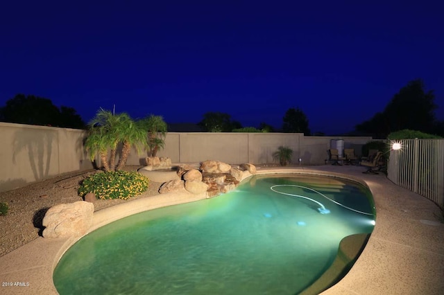 pool at night featuring a fenced backyard and a fenced in pool