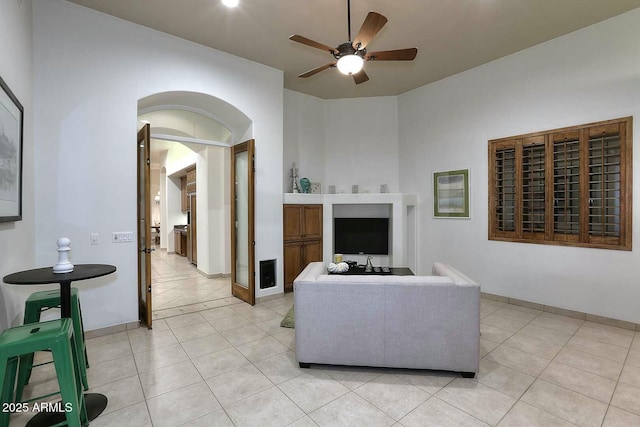 living room featuring ceiling fan, arched walkways, light tile patterned flooring, and baseboards