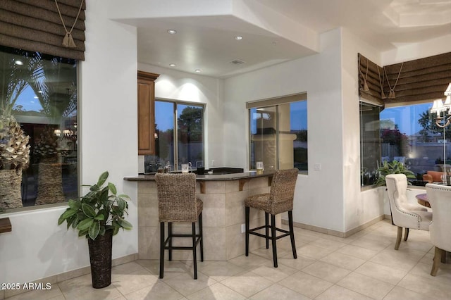 kitchen with a peninsula, recessed lighting, a breakfast bar, light tile patterned flooring, and dark countertops