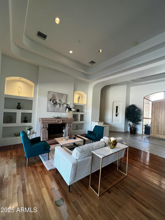 living area with visible vents, a tray ceiling, arched walkways, built in shelves, and hardwood / wood-style flooring
