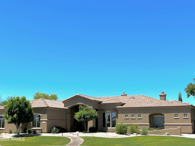 view of front of property with a chimney, a tile roof, a front lawn, and stucco siding