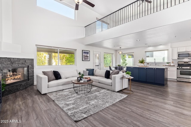 living room with dark hardwood / wood-style floors, a fireplace, ceiling fan, and a towering ceiling