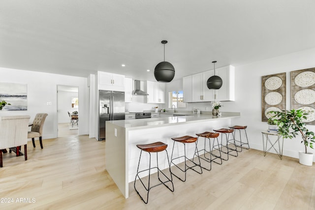 kitchen featuring light wood finished floors, stainless steel appliances, wall chimney range hood, a peninsula, and a kitchen breakfast bar