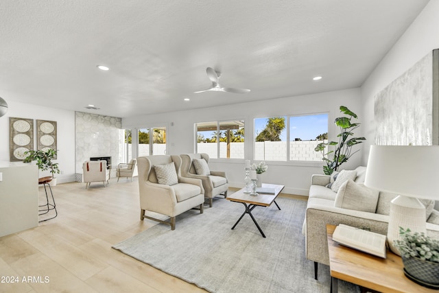 living room with a textured ceiling, ceiling fan, light wood-type flooring, and a fireplace