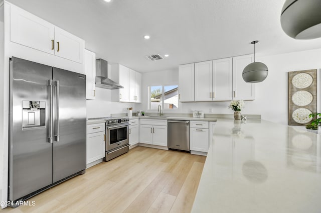 kitchen with visible vents, wall chimney exhaust hood, stainless steel appliances, light wood-style floors, and a sink