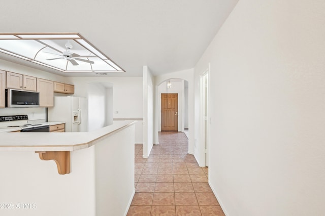 kitchen with white refrigerator with ice dispenser, ceiling fan, light tile patterned floors, electric range oven, and a kitchen bar