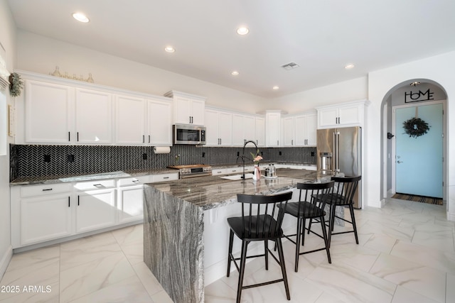 kitchen with stainless steel appliances, an island with sink, and white cabinets