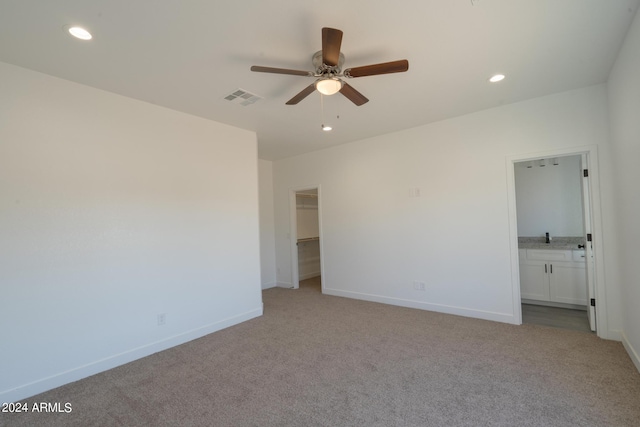 unfurnished bedroom with ceiling fan, a closet, a spacious closet, ensuite bath, and carpet