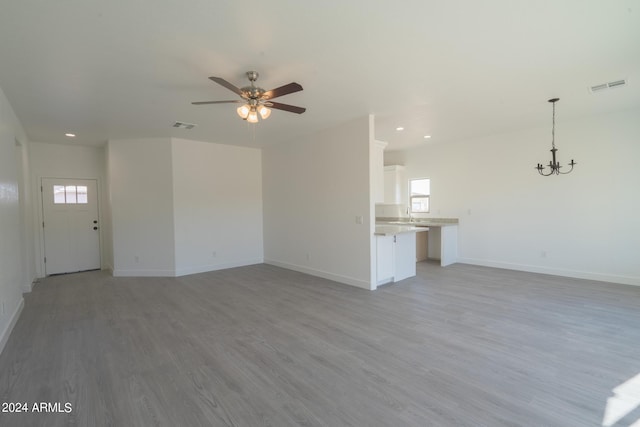 unfurnished living room with plenty of natural light, ceiling fan with notable chandelier, and light hardwood / wood-style floors