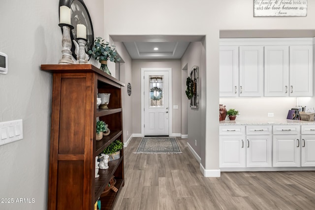 entryway with recessed lighting, a raised ceiling, light wood-style flooring, and baseboards