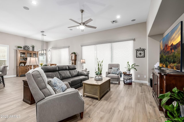 living room featuring baseboards, visible vents, light wood finished floors, and ceiling fan with notable chandelier