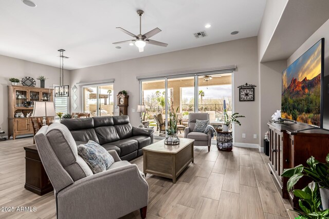 living room with light wood-style floors, a wealth of natural light, baseboards, and ceiling fan with notable chandelier