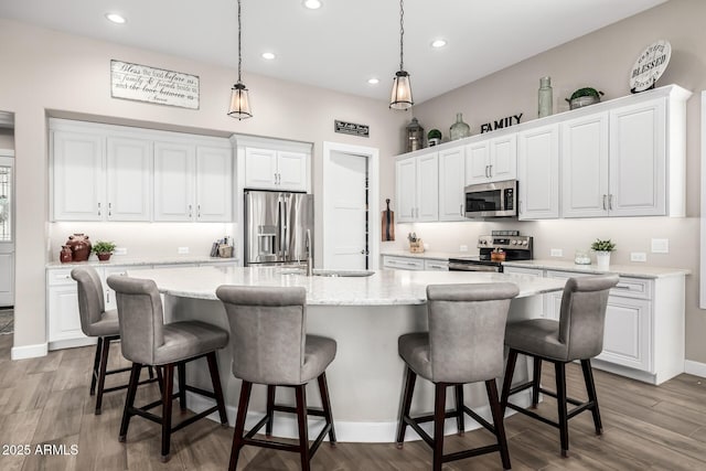 kitchen featuring stainless steel appliances, dark wood-type flooring, a kitchen island with sink, white cabinets, and a sink