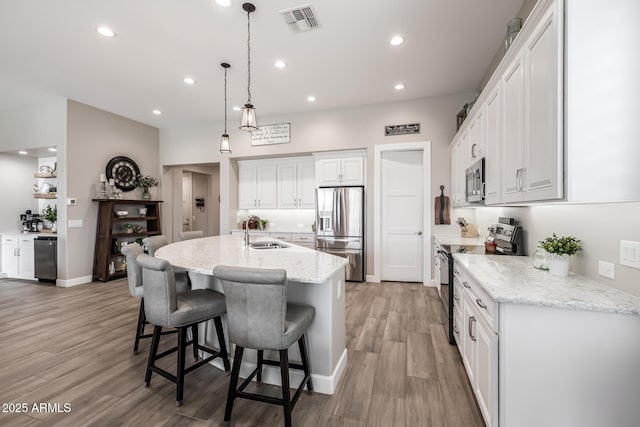 kitchen with a sink, visible vents, white cabinetry, appliances with stainless steel finishes, and a kitchen bar