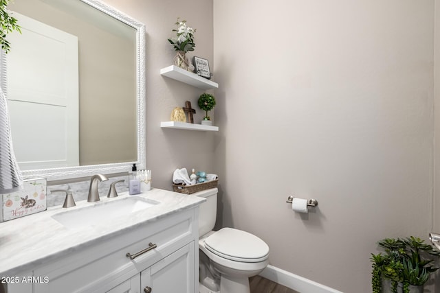 half bathroom with vanity, toilet, and baseboards