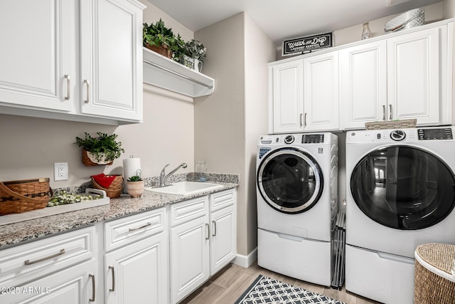 laundry room with light wood-type flooring, cabinet space, washing machine and dryer, and a sink