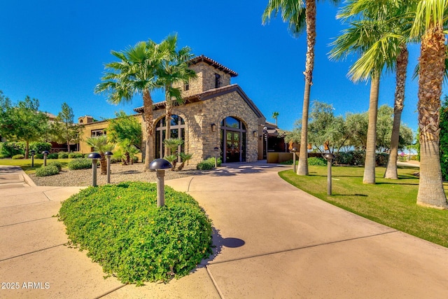 mediterranean / spanish house with stone siding, a front lawn, and concrete driveway