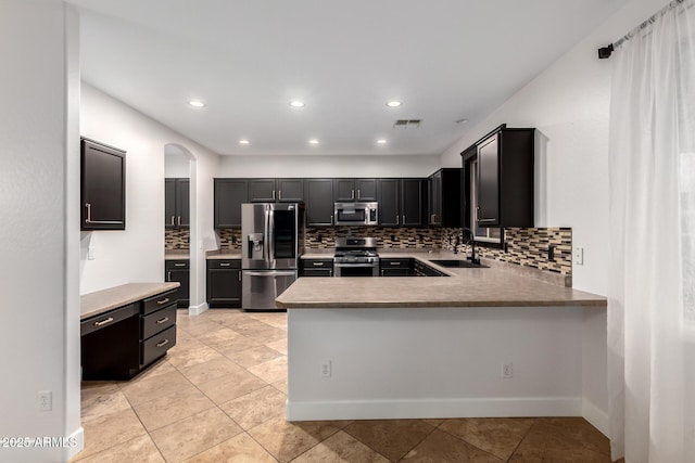 46065 W Meadows Ln, Maricopa, AZ 85139 - kitchen featuring stainless steel appliances, decorative backsplash, arched walkways, dark cabinets, and a peninsula