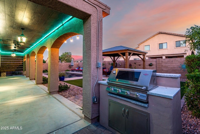 46065 W Meadows Ln, Maricopa, AZ 85139 - patio terrace at dusk featuring a gazebo, a fenced backyard, a patio, and exterior kitchen