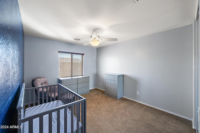 carpeted bedroom with a ceiling fan, a nursery area, visible vents, and baseboards