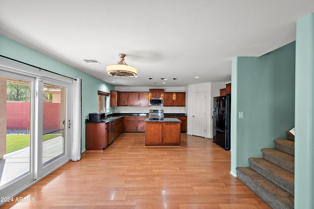 kitchen with stainless steel appliances, a kitchen island, brown cabinets, dark countertops, and pendant lighting