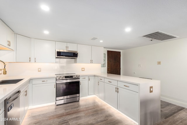 kitchen with kitchen peninsula, white cabinetry, stainless steel appliances, and dark wood-type flooring