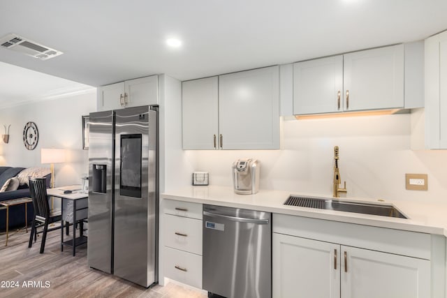 kitchen featuring appliances with stainless steel finishes, sink, light hardwood / wood-style floors, white cabinets, and crown molding