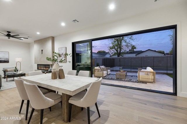 dining space with ceiling fan, a large fireplace, and light wood-type flooring