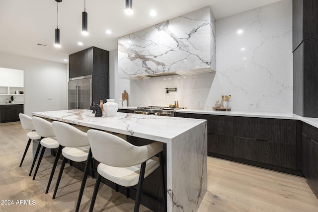 kitchen featuring decorative light fixtures, a kitchen island, light hardwood / wood-style flooring, a breakfast bar area, and light stone counters