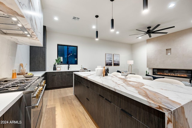 kitchen with pendant lighting, a large fireplace, light wood-type flooring, custom range hood, and ceiling fan