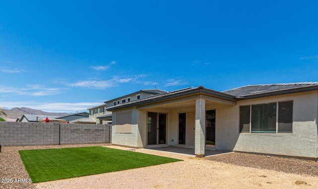 rear view of property featuring a patio, a mountain view, fence, a lawn, and stucco siding