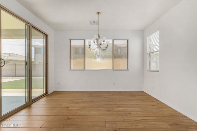 unfurnished dining area with light wood-type flooring, visible vents, baseboards, and an inviting chandelier